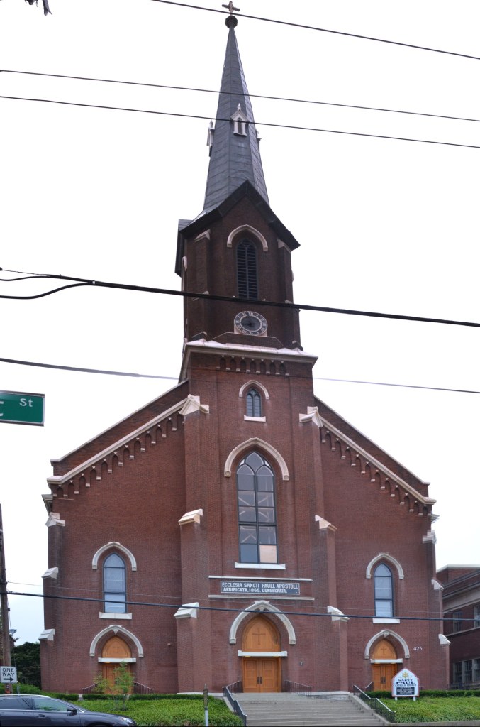 Vertical panorama of the brick Gothic Revival facade of St. Paul Catholic Church on West Short Street, from the three arched doorways to the tower and spire