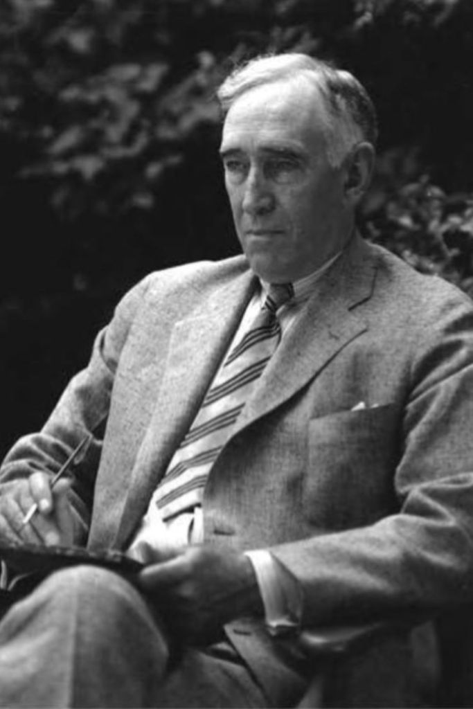 Black-and-white photograph of a white-haired Frank L. McVey seated outdoors in a light suit and striped tie, holding a pen over a writing board.
