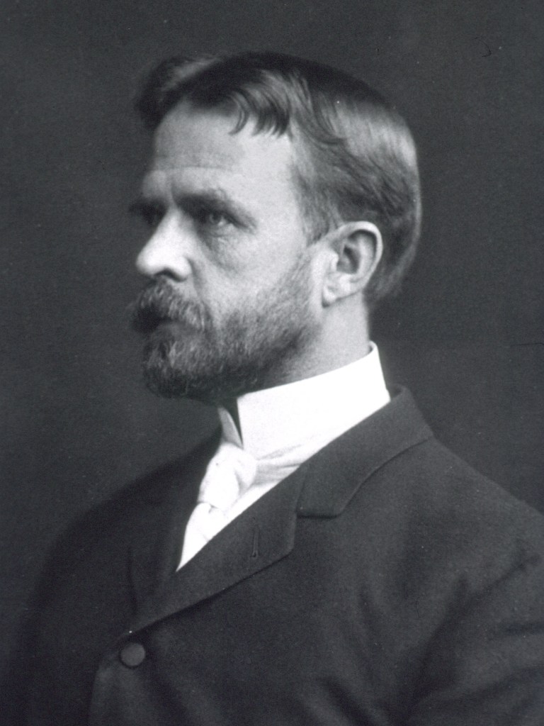 Black-and-white studio portrait of Thomas Hunt Morgan in profile, with a full beard, dark suit and high white collar.